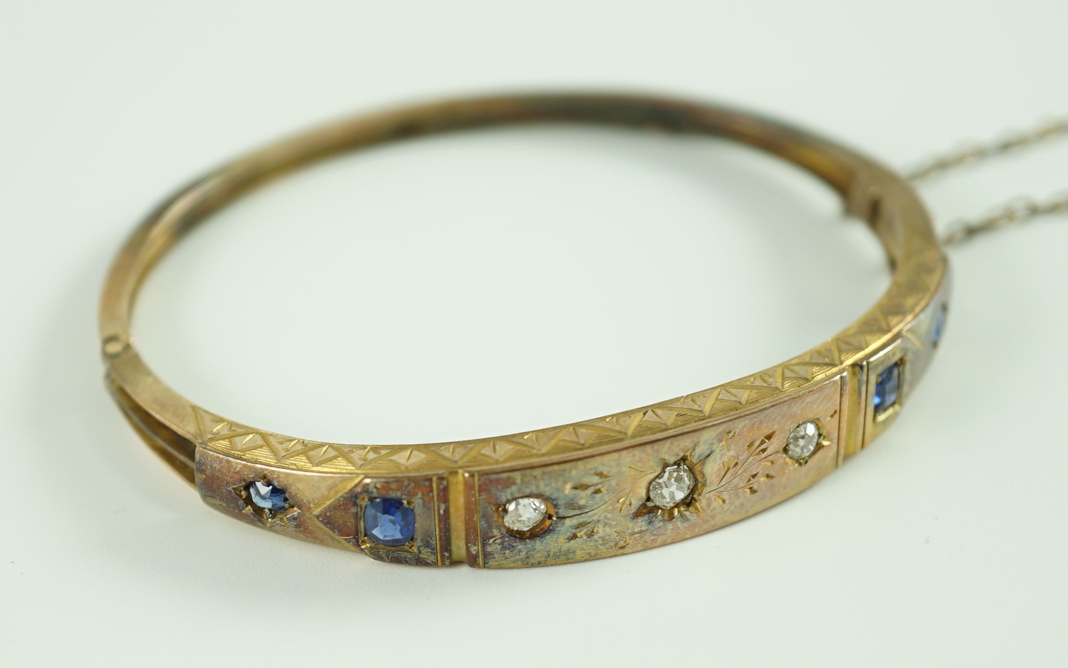 A late Victorian engraved gold, gypsy set three stone diamond and four stone sapphire set hinged bangle